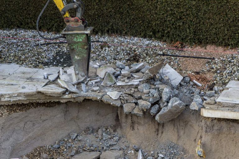 on a private construction site, a swimming pool is being dismantled by an excavator