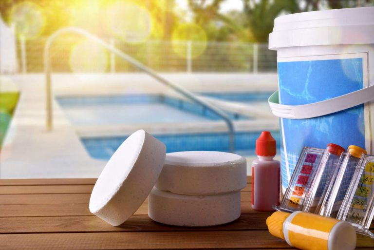 Swimming pool service and equipment with chemical cleaning products and tools on wood table and pool background. Horizontal composition. Front view